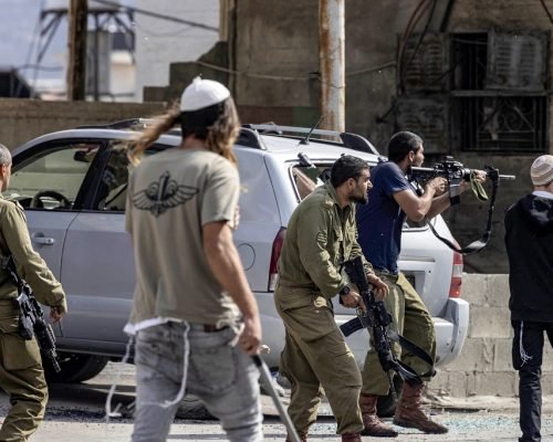 Israeli settlers fire at Palestinians (unseen) while an Israeli soldier (L) stands by during clashes in the town of Huwara in the occupied West Bank on October 13, 2022. (Photo by Oren ZIV / AFP)